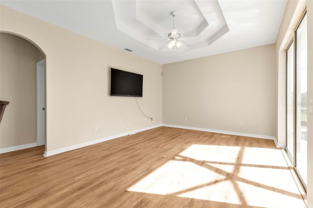 empty room with ceiling fan, a healthy amount of sunlight, a tray ceiling, and light hardwood / wood-style flooring