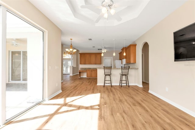 kitchen with a raised ceiling, pendant lighting, white appliances, light hardwood / wood-style floors, and a kitchen bar