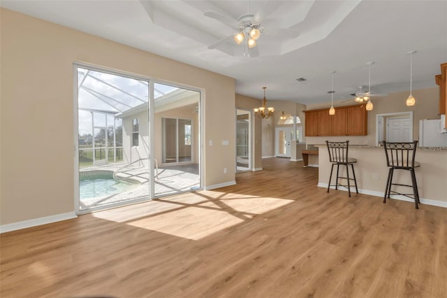 unfurnished living room featuring a raised ceiling, ceiling fan with notable chandelier, and light wood-type flooring