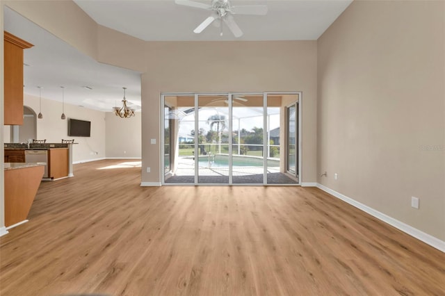 unfurnished living room with ceiling fan with notable chandelier and light hardwood / wood-style flooring