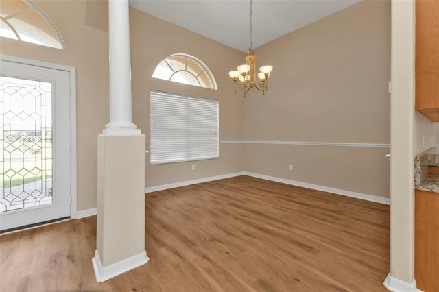 unfurnished dining area with hardwood / wood-style flooring, ornate columns, and a chandelier