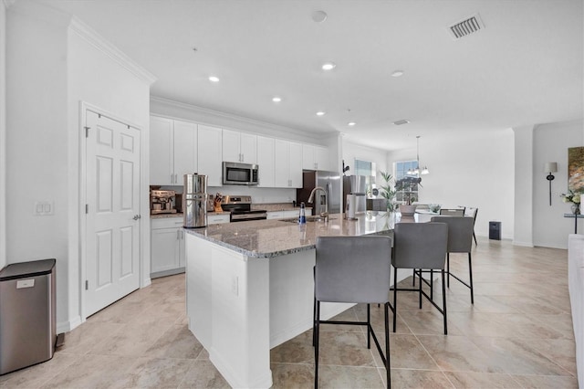 kitchen featuring a center island with sink, appliances with stainless steel finishes, ornamental molding, a kitchen bar, and white cabinets