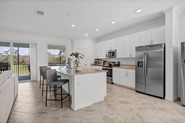 kitchen featuring stainless steel appliances, a center island with sink, light stone counters, crown molding, and white cabinetry