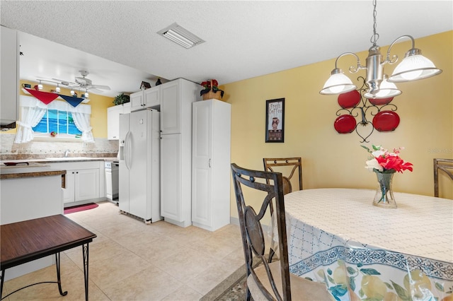 kitchen with white fridge with ice dispenser, pendant lighting, ceiling fan with notable chandelier, and white cabinets