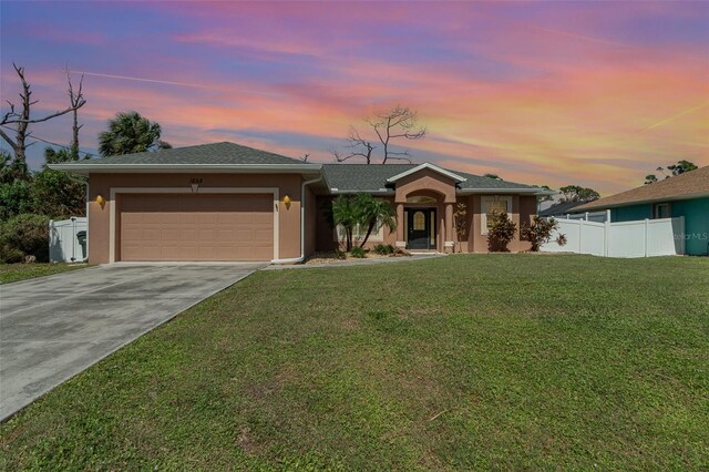 ranch-style home featuring a lawn, driveway, stucco siding, and an attached garage