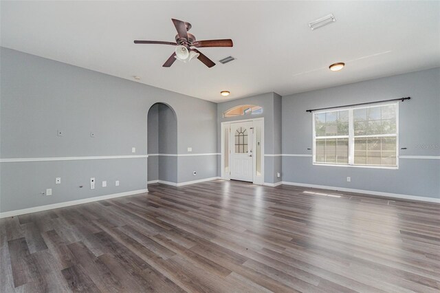 unfurnished living room featuring wood finished floors, visible vents, arched walkways, a ceiling fan, and baseboards