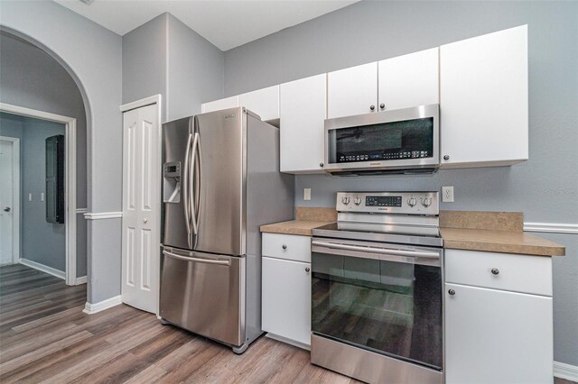 kitchen with arched walkways, light countertops, light wood finished floors, and appliances with stainless steel finishes