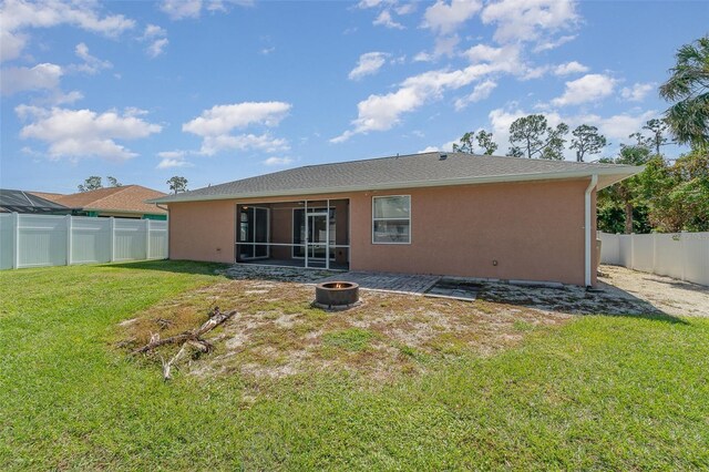 rear view of property featuring an outdoor fire pit, a sunroom, stucco siding, a lawn, and a fenced backyard