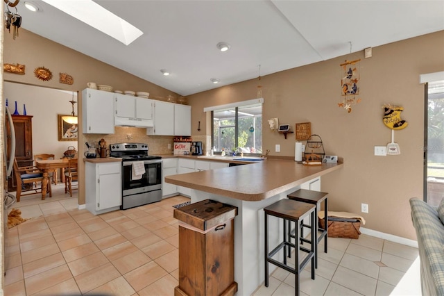 kitchen featuring a breakfast bar area, kitchen peninsula, stainless steel electric range, lofted ceiling with skylight, and white cabinetry