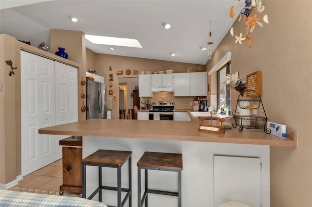 kitchen with kitchen peninsula, stainless steel appliances, a breakfast bar, vaulted ceiling with skylight, and white cabinets