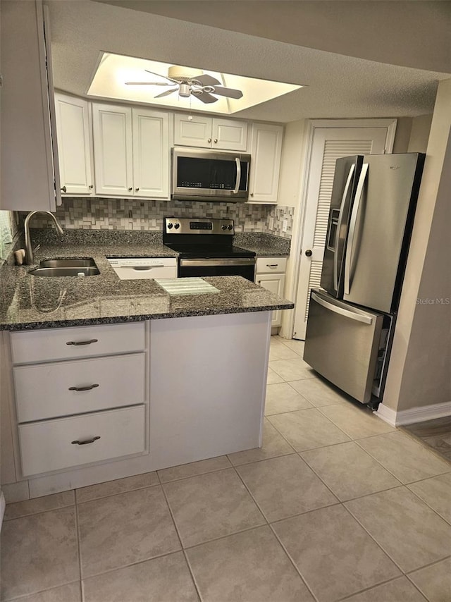 kitchen featuring sink, light tile patterned floors, stainless steel appliances, white cabinets, and dark stone counters