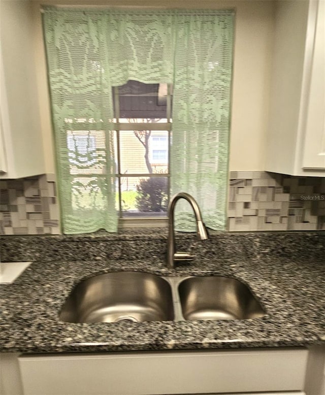 details featuring sink, white cabinets, tasteful backsplash, and dark stone countertops