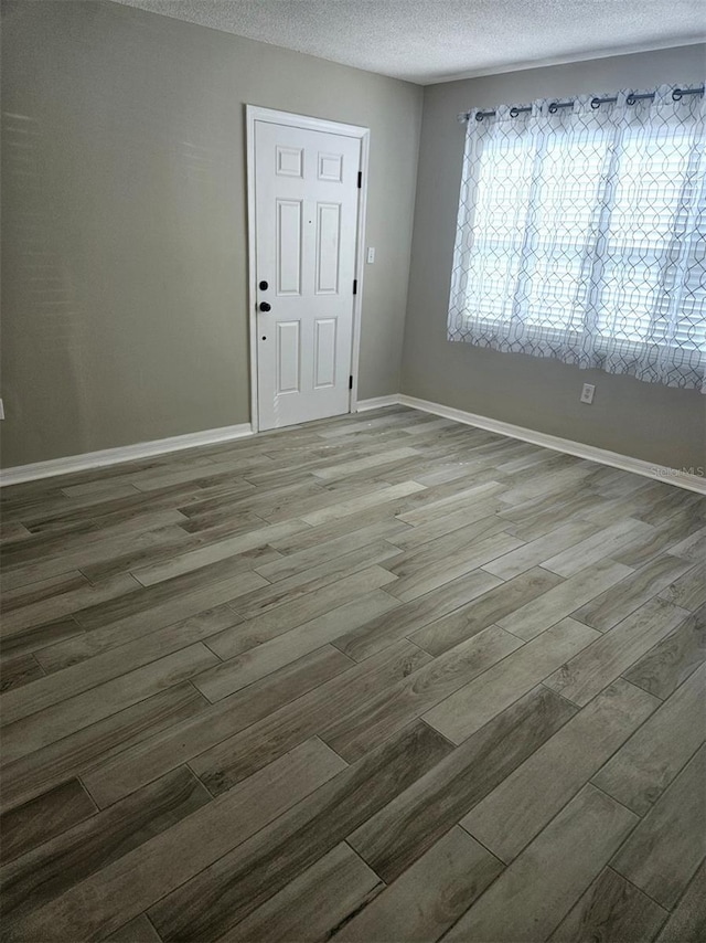 spare room featuring a textured ceiling, baseboards, and wood finished floors