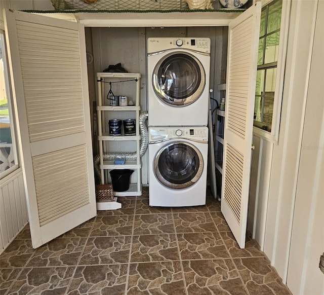 laundry room with stone floors, laundry area, and stacked washer / dryer