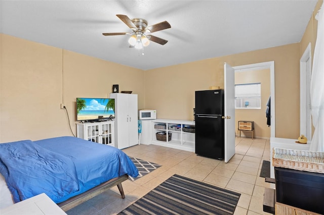 bedroom with light tile patterned flooring, black refrigerator, and ceiling fan