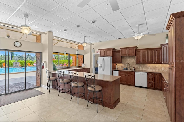 kitchen featuring decorative backsplash, a kitchen bar, light tile patterned flooring, sink, and white appliances