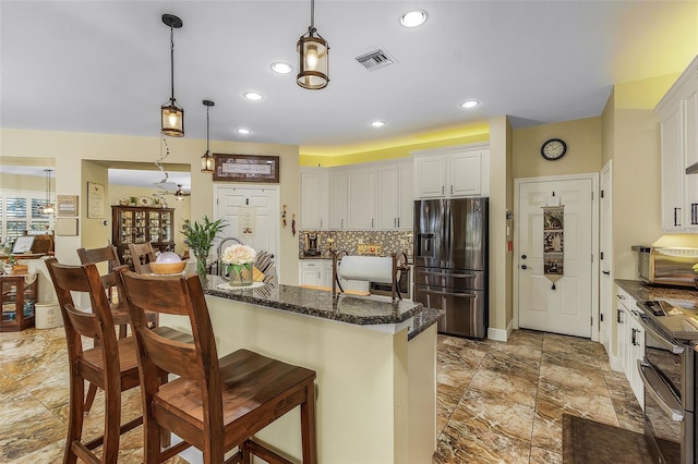 kitchen featuring a kitchen breakfast bar, dark stone countertops, white cabinets, decorative light fixtures, and appliances with stainless steel finishes