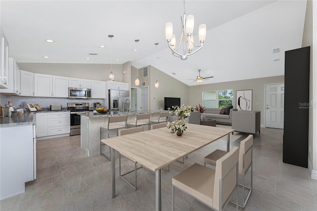 dining area featuring high vaulted ceiling and ceiling fan with notable chandelier