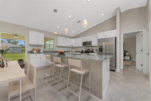 kitchen featuring sink, an island with sink, stainless steel appliances, white cabinets, and a breakfast bar