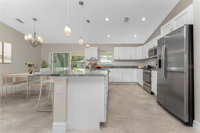 kitchen with appliances with stainless steel finishes, a kitchen bar, decorative light fixtures, white cabinets, and a center island with sink