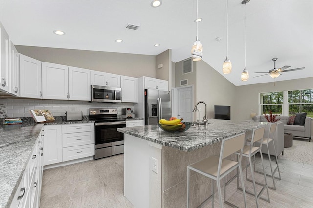 kitchen with appliances with stainless steel finishes, white cabinets, a kitchen island with sink, and a kitchen bar