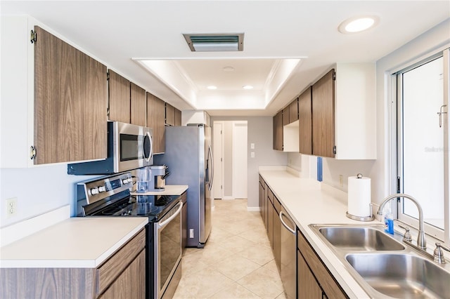 kitchen with sink, appliances with stainless steel finishes, light tile patterned flooring, and a raised ceiling