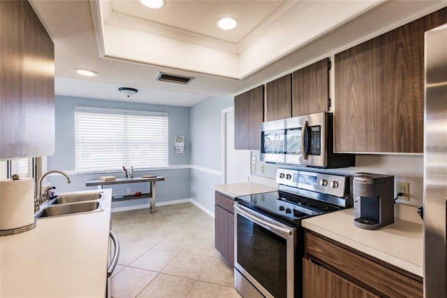 kitchen featuring appliances with stainless steel finishes, a tray ceiling, light tile patterned flooring, crown molding, and sink