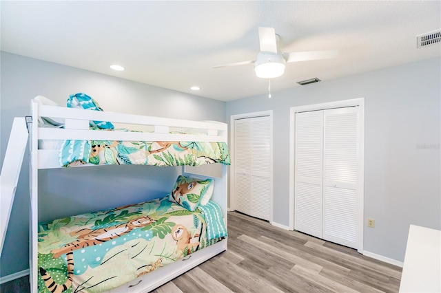 bedroom featuring two closets, light wood-type flooring, and ceiling fan