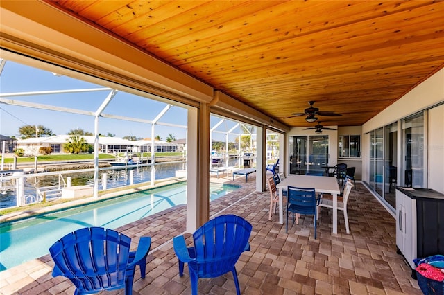 view of patio with ceiling fan, a water view, and glass enclosure