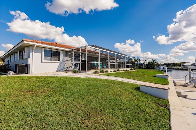 rear view of property featuring a water view, a lanai, and a lawn