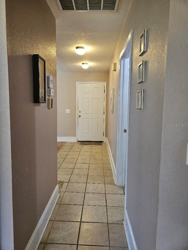 hall with a textured ceiling and light tile patterned floors