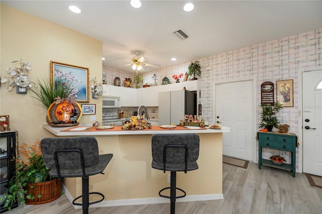 kitchen featuring light hardwood / wood-style floors, kitchen peninsula, white cabinetry, and a breakfast bar area