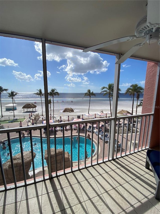 balcony featuring a view of the beach, a water view, and ceiling fan