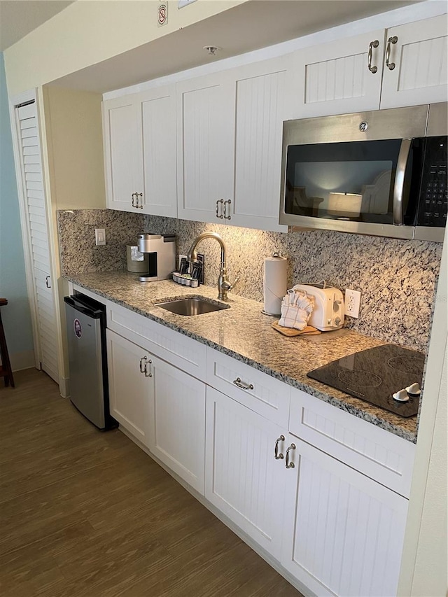 kitchen featuring hardwood / wood-style floors, tasteful backsplash, white cabinetry, black electric stovetop, and sink