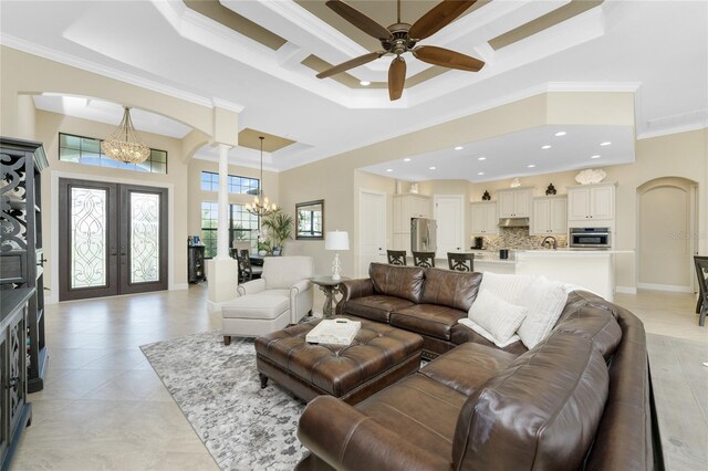 living room with ornamental molding, ceiling fan with notable chandelier, light tile patterned floors, a raised ceiling, and french doors