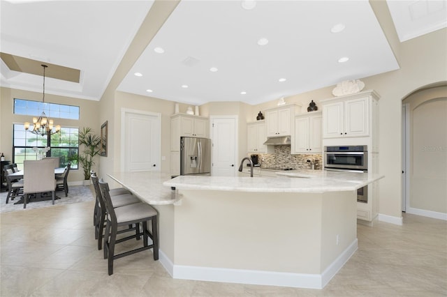 kitchen featuring a kitchen bar, stainless steel appliances, a large island with sink, and light stone countertops