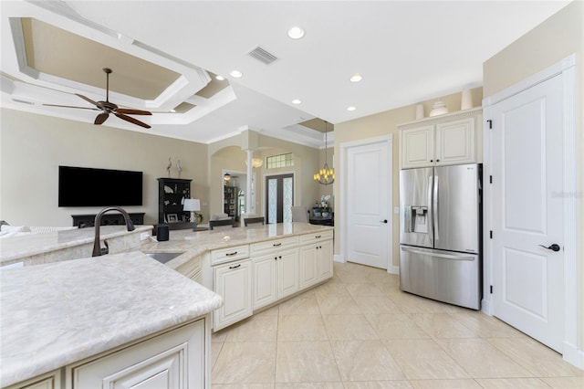 kitchen with sink, light stone counters, ceiling fan with notable chandelier, stainless steel fridge with ice dispenser, and pendant lighting