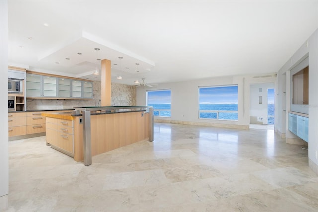 kitchen with a kitchen island, decorative backsplash, stainless steel microwave, hanging light fixtures, and light brown cabinetry