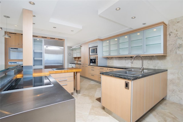 kitchen with light brown cabinets, kitchen peninsula, sink, built in appliances, and decorative light fixtures