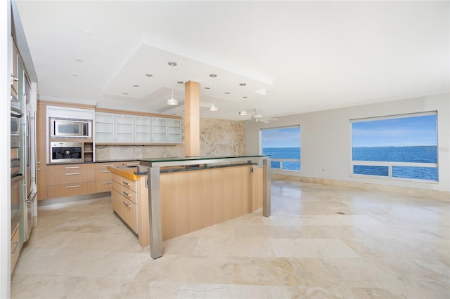 kitchen featuring light brown cabinetry, appliances with stainless steel finishes, a kitchen island, decorative light fixtures, and a water view