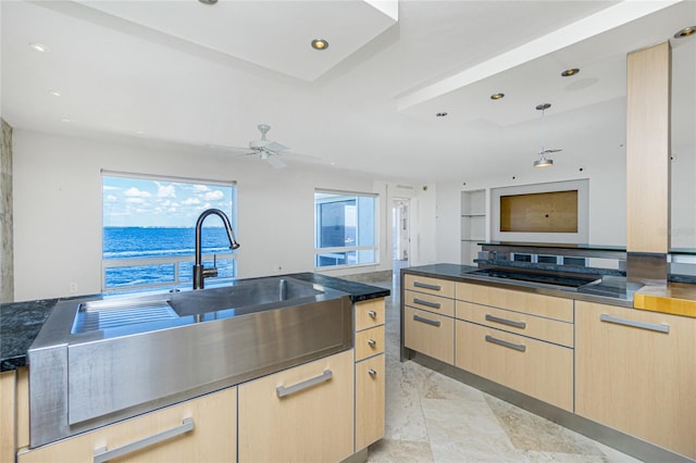 kitchen featuring stovetop, light brown cabinetry, a water view, and ceiling fan