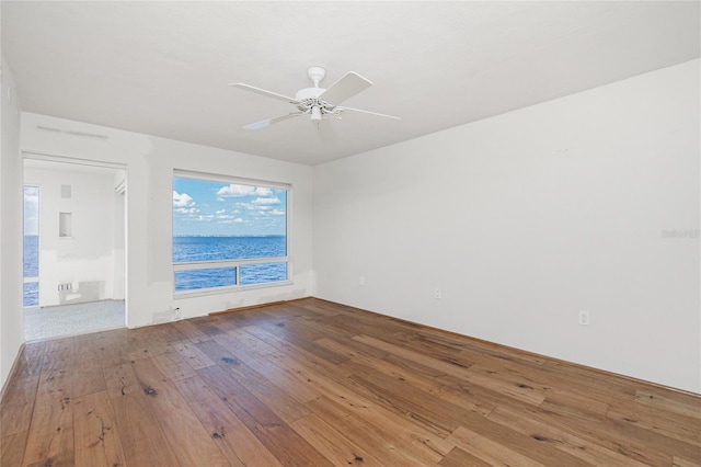 empty room with a water view, hardwood / wood-style flooring, and ceiling fan