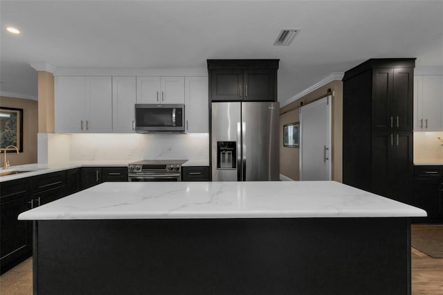 kitchen with appliances with stainless steel finishes, a barn door, a center island, and sink