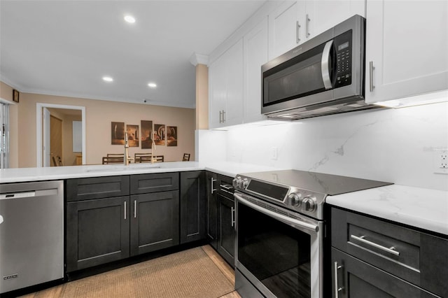 kitchen with white cabinetry, kitchen peninsula, decorative backsplash, appliances with stainless steel finishes, and ornamental molding