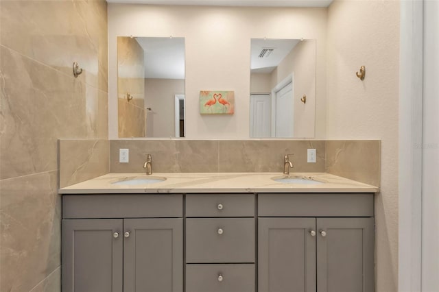 bathroom featuring double vanity, backsplash, a sink, and visible vents
