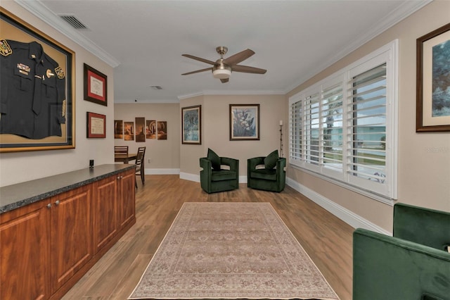 sitting room with ceiling fan, light wood-type flooring, and crown molding