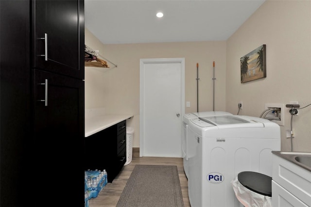 laundry area with washing machine and clothes dryer, cabinets, and light hardwood / wood-style floors