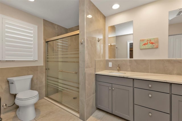 bathroom with tile patterned floors, toilet, a shower with shower door, and tile walls