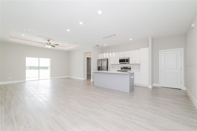 kitchen with an island with sink, stainless steel appliances, light wood-type flooring, white cabinetry, and ceiling fan