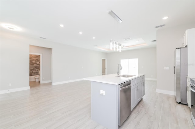 kitchen featuring appliances with stainless steel finishes, sink, an island with sink, hanging light fixtures, and light hardwood / wood-style floors